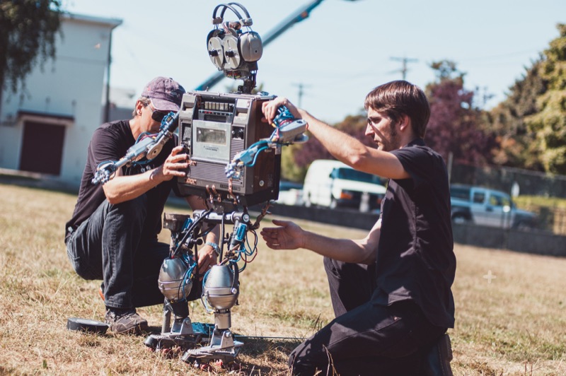 Two people outdoors hands-on with an in-progress robotic build, wiring exposed — hardening a prototype into a working system.